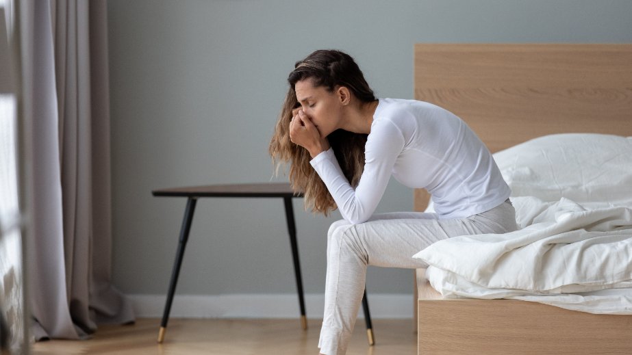 stresszes fiatal nő ágy szélén ül 