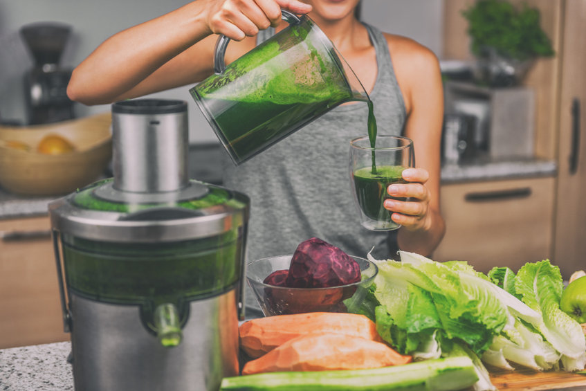 Nő zöldségekből elkészült smoothiet green juicet önti át a pohárba 